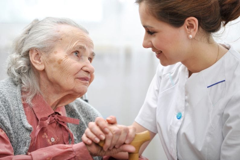 Recruiting CNAs. An older woman and a young CNA hold hands and smile at each other.