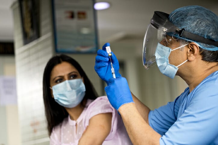 Vaccine hesitancy. A woman watches cautiously while a nurse prepares a vaccine.