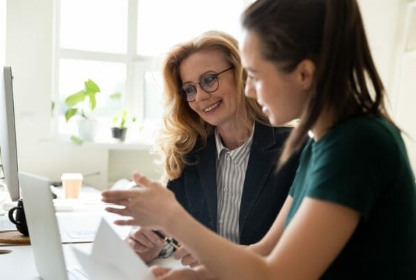 Two employees work together at a computer, reviewing their digital talent management