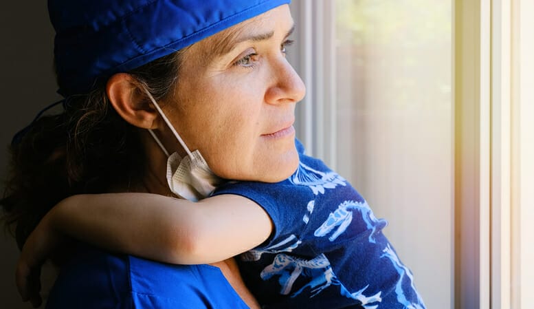 Healthcare funding. A healthcare worker holds a young child and looks pensive.