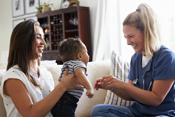 Benefits for nurses. A young healthcare worker plays with a baby who is being held by another young woman.