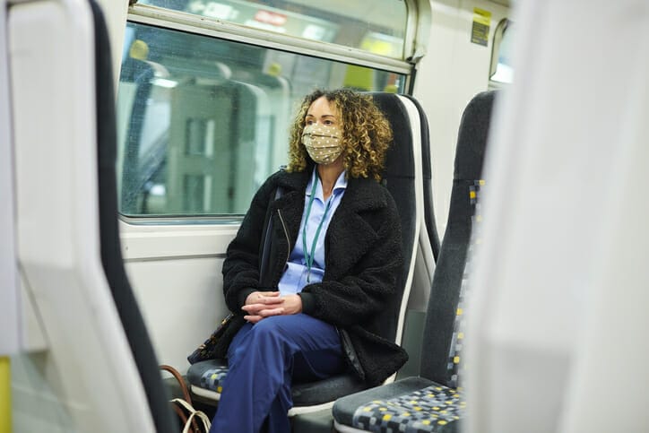 A travel LPN sits on a train with a mask on