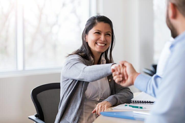 A smiling businesswoman shakes hands with a man who is out of focus during healthcare onboarding.
