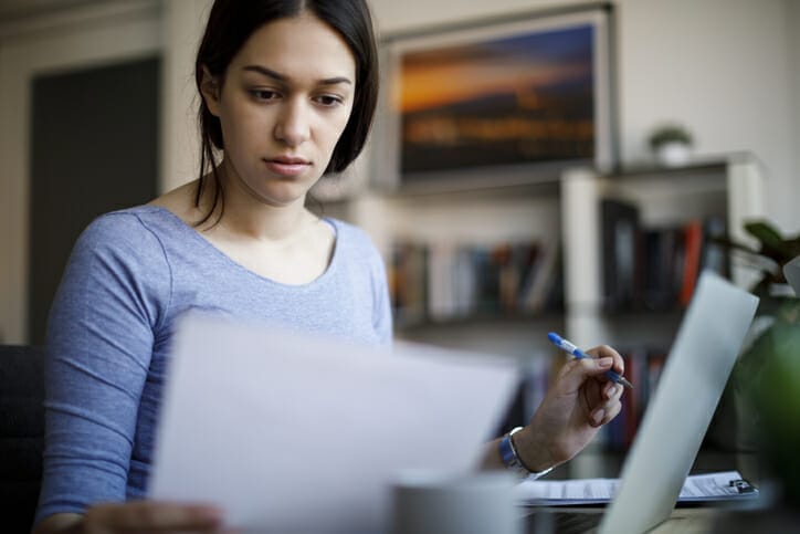 Hireology vs Apploi. A woman works on her computer and looks at a piece of paper, comparing two options.